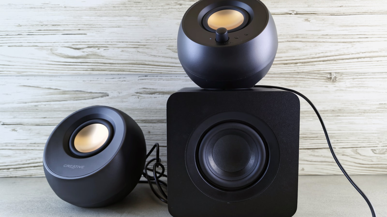 Zwei kugelförmige kleine Lautsprecher und ein würfelförmiger Subwoofer auf heller Fläche