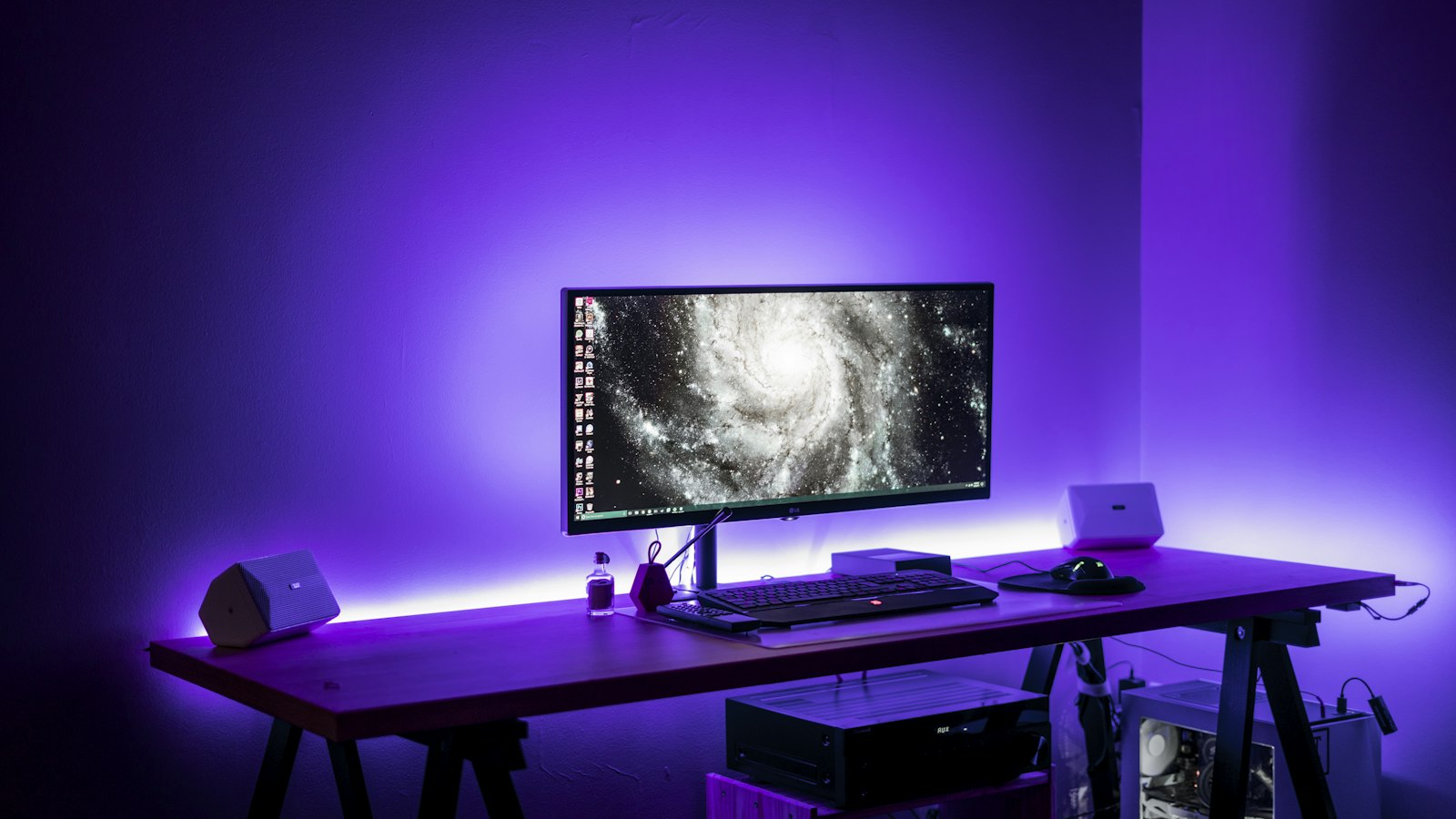 ASUS ROG Gjallar am PC: Was die Gaming-Soundbar am Schreibtisch taugt Breiter Schreibtisch mit Monitor und zwei kleinen Lautsprechern in violettem Licht